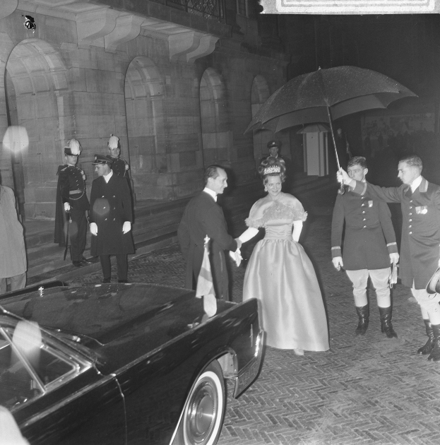 Schwarzes und weißes Foto von Queen Elizabeth II. und Prinz Philip, Duke of Edinburgh, bei der Ankunft im Buckingham Palace in formeller Kleidung, wobei die Queen einen Blumenstrauß hält und der Duke einen Schirm hält, vor einem Hintergrund mit einem gebogenen Gebäude.