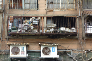 Wohngebäude mit Fenstern, Eisengittern, Klimaanlagen, Rohren und Kabeln an der Außenseite.