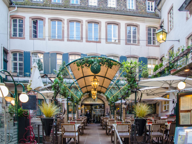 Ein Innenhof in Frankfurt, Deutschland, mit Tischen, Stühlen, Pflanzen, Sonnenschirmen und einem Gebäude mit Fenstern im Hintergrund.