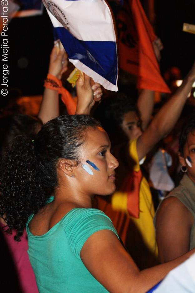 Frauen in grünen T-Shirts bei einer Demonstration, die weiße Zettel in den Händen halten, mit vielen anderen Mädchen im Hintergrund.