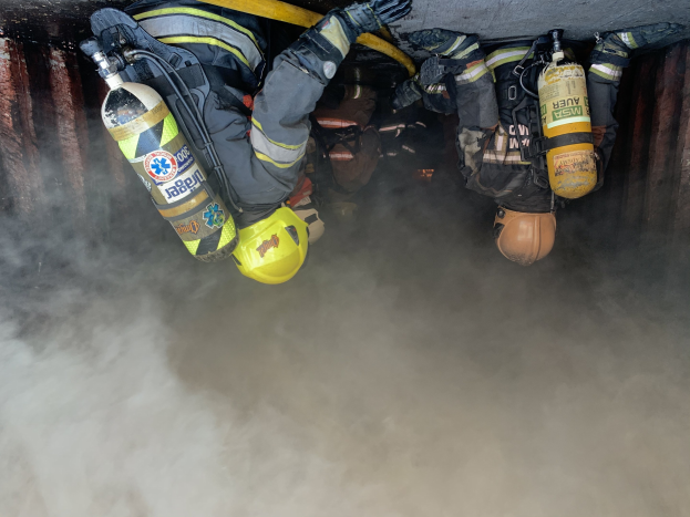 Feuerwehrleute in Schutzausrüstung löschen ein großes Feuer in einem raucherfüllten Tunnel mit Schläuchen.