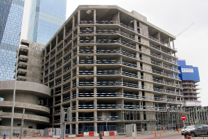 Großes Bauprojekt in einer Stadt mit Wolkenkratzern, Fahrzeugen, Fußgängern, Verkehrsinfrastruktur und Kränen unter einem klaren Himmel.
