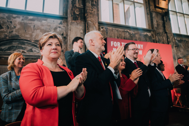 Eine Gruppe von Menschen, die vor einer Menge jubeln und ein Banner mit der Aufschrift 'Wahlsieg' im Hintergrund halten.
