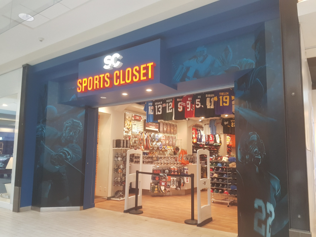 Sportbekleidungsgeschäft in einem Einkaufszentrum mit einem "SC Sports Closet"-Schild, gläserne Eingangstür, hängende Kleidung, ordentliche Regale und Deckenbeleuchtung.