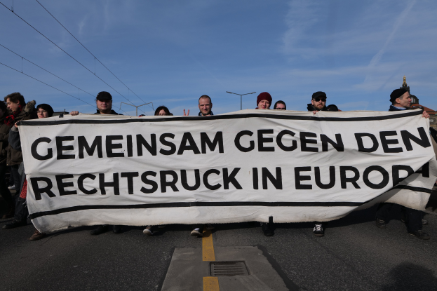 Gruppe von Menschen auf einer Straße mit einem Transparent "Gemeinsam gegen den Rechtsruck in Europa" bei einer Protestaktion gegen die Europäische Union, mit Straßeninfrastruktur und Gebäuden im Hintergrund.