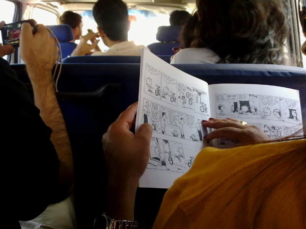 Ein Nahaufnahme eines Menschen mit einer Armbanduhr und einem Ring am Handgelenk, mit einem Buch und einem Gadget im Hintergrund, in einem Fahrzeug.