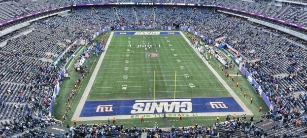 Ein volles Fußballstadion mit Spielern auf dem Feld, Torpfosten und Texttafeln, umgeben von Reihen leerer Sitze.