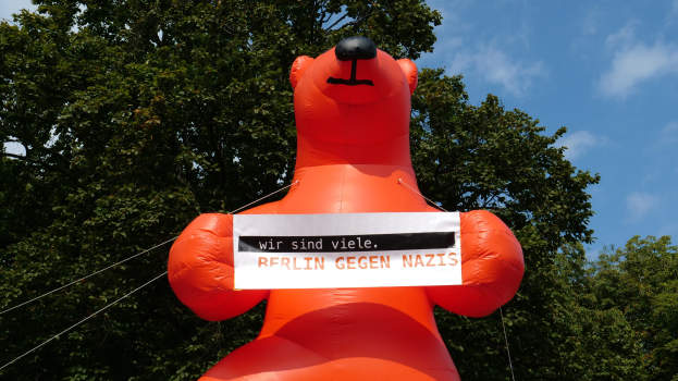 Ein Luftbär mit einem Schild "Berlin gegen Nazis" vor Bäumen und Wolken im Hintergrund.