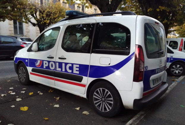 Polizeifahrzeug auf einer von Gebäuden, Bäumen und verstreuten Laub gesäumten Straße geparkt.