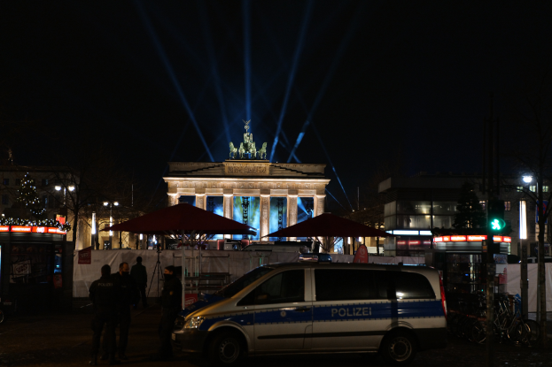 Ein Polizeiwagen parkt vor dem Brandenburger Tor in Berlin bei Nacht, umringt von einigen Menschen und verschiedenen Gegenständen, die in der Gegend verstreut sind.