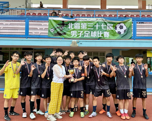 Gruppe junger Männer in Fußballtrikots auf einem Feld mit einem Pokal und Medaillen stehend, im Hintergrund ein Banner 'Yokohama U-16 Jungen Fußballteam'
