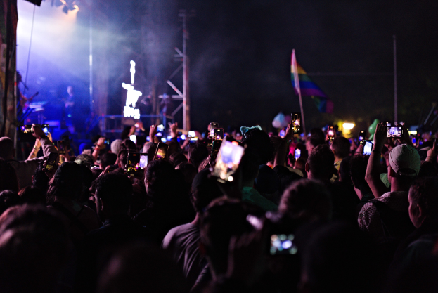 Menge bei einem Konzert mit beleuchteten Handys in der Luft, umgeben von Stangen und einer Fahne auf der Bühne