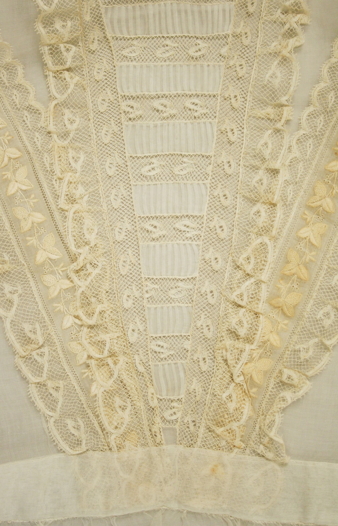 Nahaufnahme eines weißen Kleides mit detaillierter Spitzenverzierung, das zarte Muster und einen leichten, luftigen Stoff für den Sommer bietet.