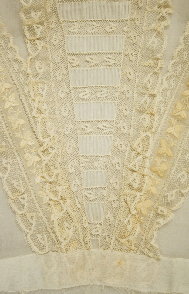 Nahaufnahme eines weißen Kleides mit detaillierter Spitzenverzierung, das zarte Muster und einen leichten, luftigen Stoff für den Sommer bietet.