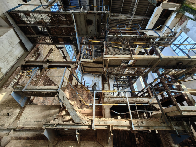 Alte Industriegebäude mit einem zentralen Metallgerüst, umgeben von verrosteten Eisenstangen, Treppen, Wänden und Fenstern, die Zeichen von Verfall und Verfall zeigen.