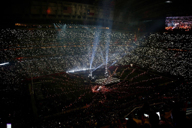 Eine große Menge in einem hell erleuchteten Stadion bei Nacht schaut auf einen Bildschirm mit den Ergebnissen der Super Bowl XLVII-Halftime-Show.