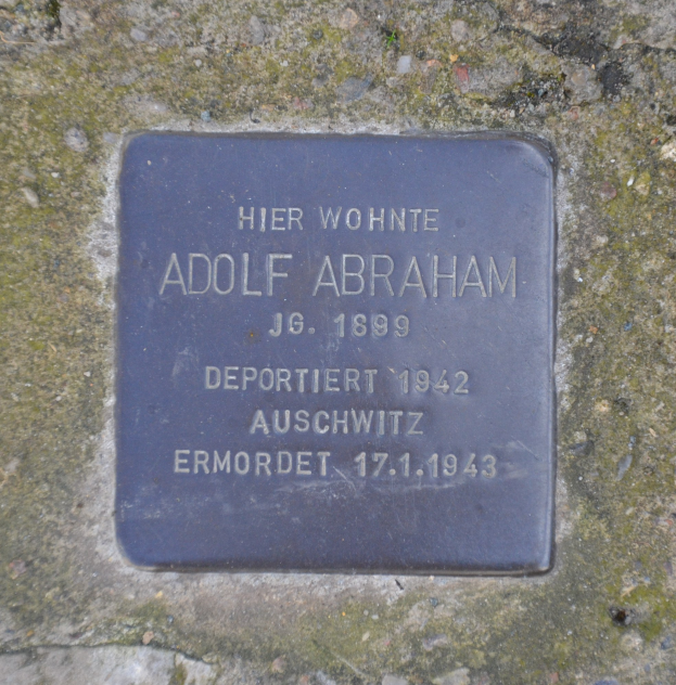 Rechteckige Plakette mit 'Adolf Abraham' auf einer Steinwand.