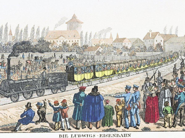 Eine Gruppe von Menschen steht um einen Zug auf Schienen herum, einige sitzen im Zug und andere auf dem Boden, vor einem Gebäude- und Baumhintergrund, mit dem Text "Ludwigs-Eisenbahn, der erste Bahnhof in Deutschland" unten.