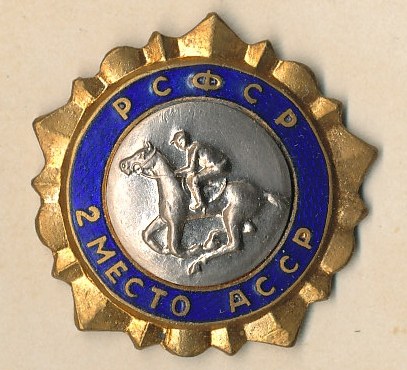 Ein gold-blauer Kreisabzeichen mit einem Pferd und Reiter in der Mitte, umgeben von Text.