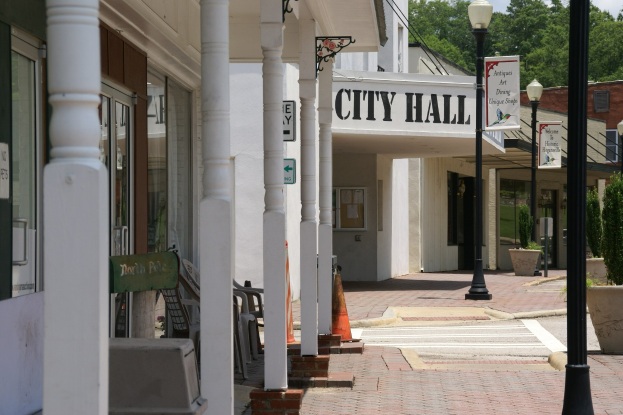 Rathaus mit umliegenden Gebäuden, Straßeninfrastruktur, Fahrzeugen und Grünflächen unter einem bewölkten Himmel.