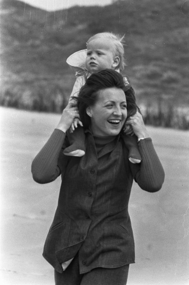 Eine Frau, die glücklich strahlend ihr Baby h├Ąlt, mit einem sanft unscharfen Hintergrund, der eine nostalgische Stimmung schafft.