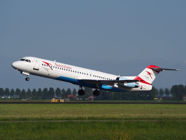 Ein Austrian-Airlines-Embraer-ERJ-190-Flugzeug startet von Frankfurt Airport, mit grünem Gras darunter und Bäumen und Gebäuden im Hintergrund unter einem sichtbaren Himmel.