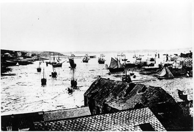 Ein Schwarz-Weiß-Foto von Booten im Wasser mit Häusern auf der rechten Seite und einer Brücke im Hintergrund, mit dem Text "Port Saint Lucie" unten.