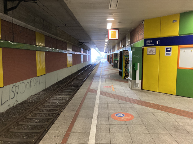 Ein Bahnsteig mit einem Zug auf den Schienen, beleuchtet von Deckenlampen, mit Graffiti an der linken Wand und ein paar Gegenständen auf der rechten Seite, identifiziert als Berlin Hauptbahnhof in Berlin, Deutschland.