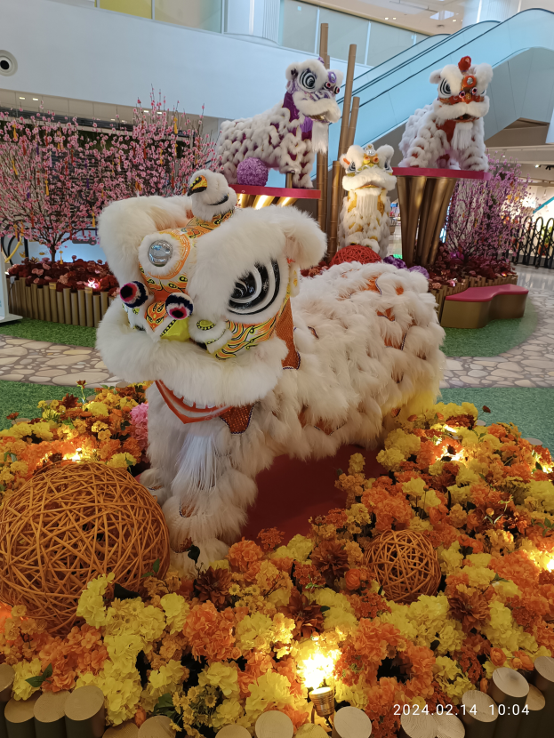 Eine festliche Chinesisches Neujahrsdisplay am Singapur Changi Airport mit Tierfiguren, Deko-Artikeln, Blumen und Lichtern, mit B├Ąumen, Pflanzen und einem Gel├Ąnder im Hintergrund.