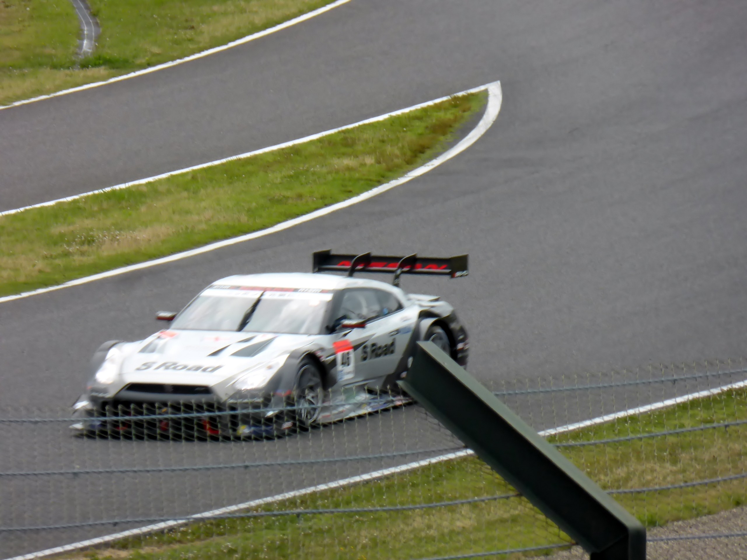 Audi R8 LMS GT3 positioniert auf der Nürburgring 24 Stunden Rennstrecke, umgeben von einem Metallzaun und grünem Gras, frontal auf der Strecke.