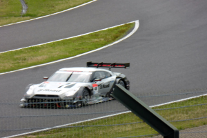 Audi R8 LMS GT3 positioniert auf der Nürburgring 24 Stunden Rennstrecke, umgeben von einem Metallzaun und grünem Gras, frontal auf der Strecke.