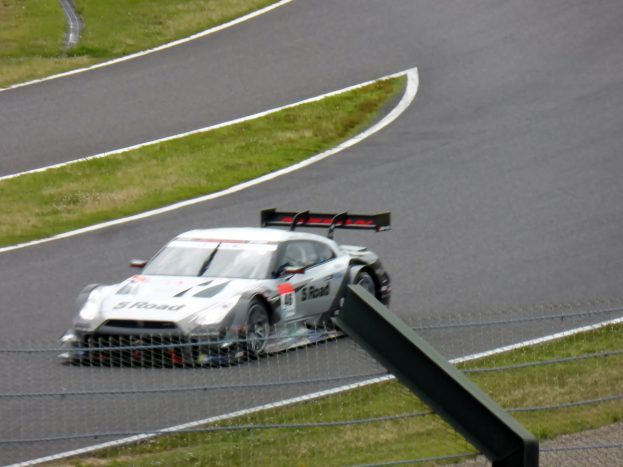 Audi R8 LMS GT3 positioniert auf der Nürburgring 24 Stunden Rennstrecke, umgeben von einem Metallzaun und grünem Gras, frontal auf der Strecke.