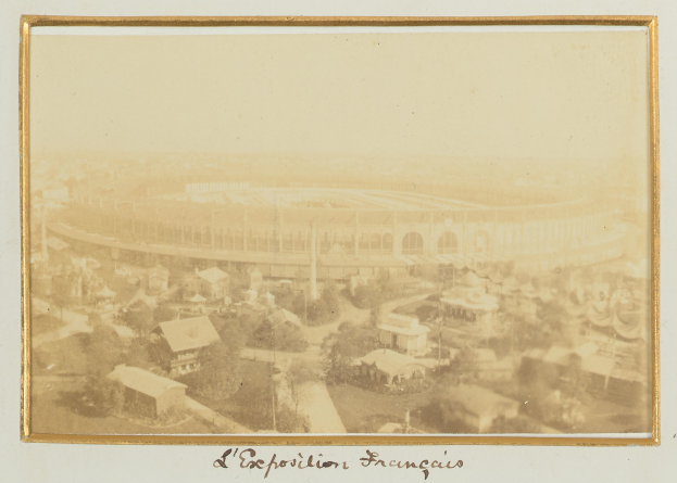 Ein altes Foto eines Stadions in einer Stadt, umgeben von Gebäuden, Bäumen und Pfählen, mit Text am unteren Rand des Bildes.