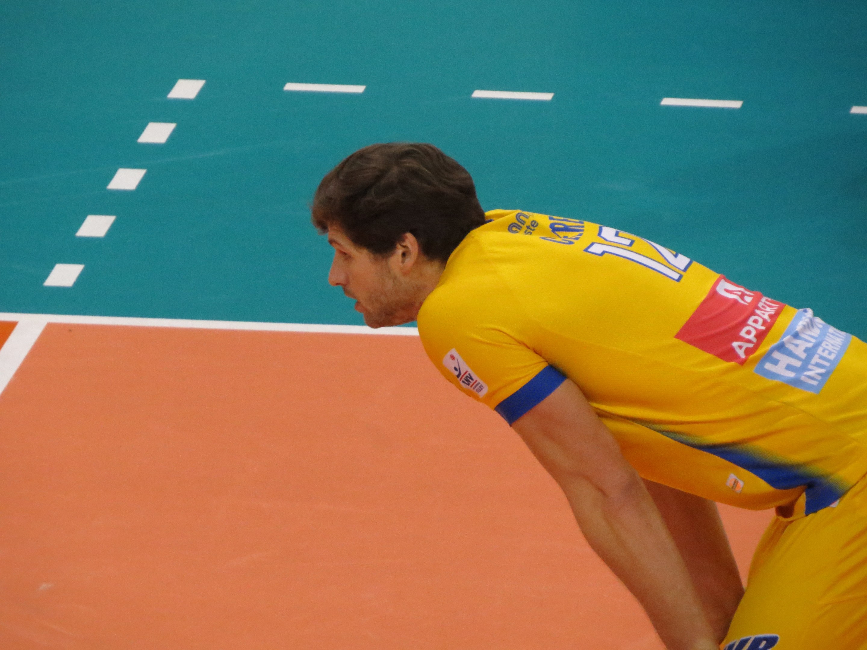 Eine professionelle Volleyballspielerin in einem gelben "Volleyball"-T-Shirt steht selbstbewusst auf einem Feld und ist bereit zum Aufschlag.