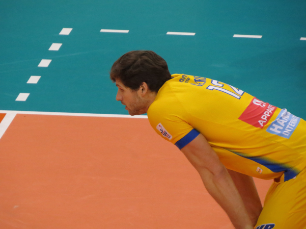 Eine professionelle Volleyballspielerin in einem gelben "Volleyball"-T-Shirt steht selbstbewusst auf einem Feld und ist bereit zum Aufschlag.