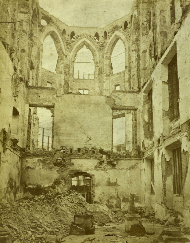 Ein altes Foto eines zerfallenen Gebäudes mit zerbrochenen Fenstern, bröckelnden Wänden und einem steinübersäten Boden.