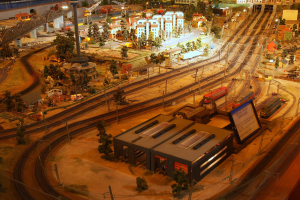 Eine detaillierte Modellbahnausstellung in einem Museum, die Gebäude, Bäume, Schienen, Fahrzeuge, Pfosten, Lichter und Platten umfasst, die eine belebte Stadtlandschaft nachahmen.