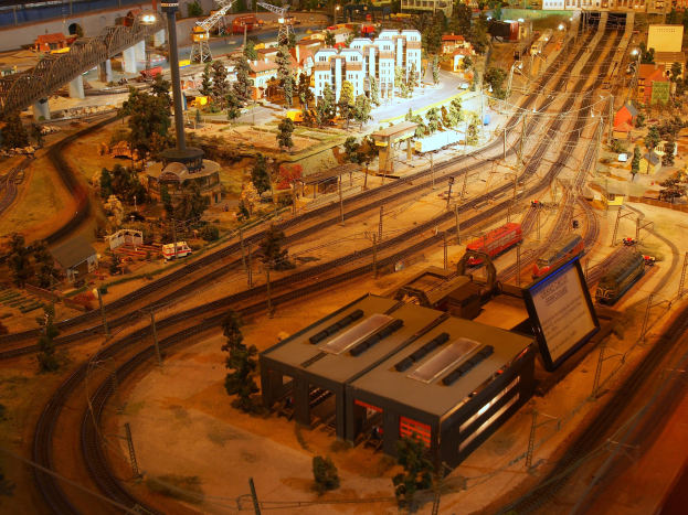 Eine detaillierte Modellbahnausstellung in einem Museum, die Gebäude, Bäume, Schienen, Fahrzeuge, Pfosten, Lichter und Platten umfasst, die eine belebte Stadtlandschaft nachahmen.