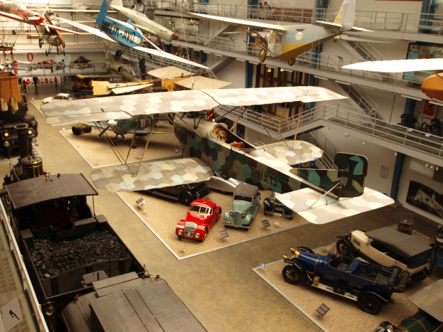 Ein großer Museumsraum voller verschiedener Flugzeuge, Fahrzeuge, Menschen, Informationsschilder und andere Ausstellungsstücke.