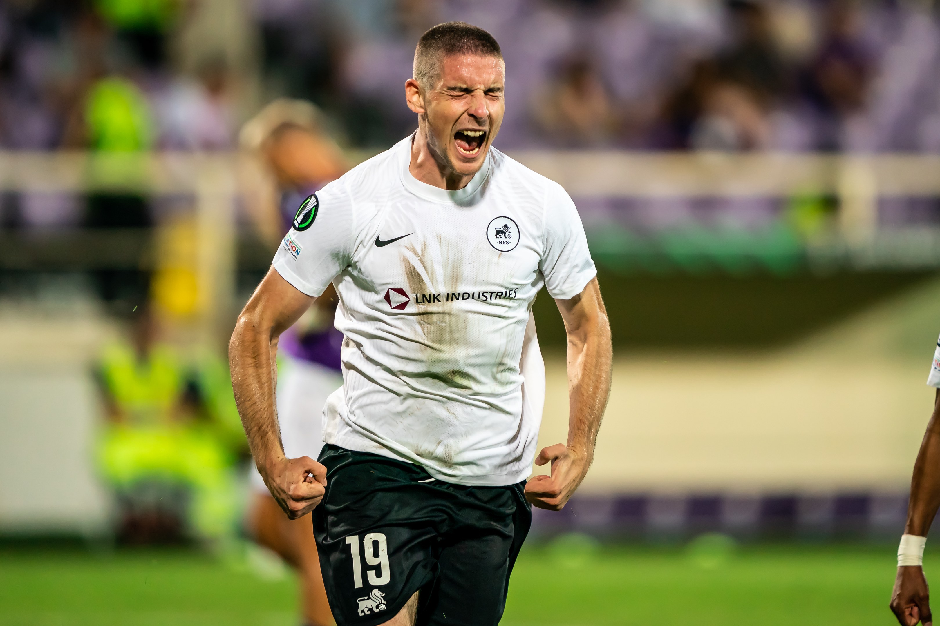 Ein Mann in weißem Hemd und schwarzen Shorts rennt auf einem Fußballfeld, umgeben von einer Gruppe von Menschen, die ein Tor während eines Spiels zwischen Leeds United und Melbourne Victory feiern.