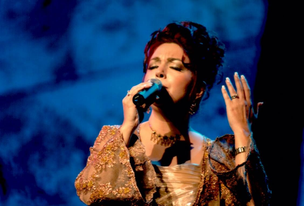Frau in goldenem Kleid, die auf der Bühne der Eurovision Song Contest in ein Mikrofon singt, mit blauem und schwarzem Hintergrund.