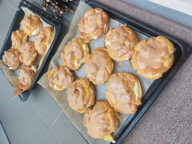 Ein Tablett mit verschiedenen dänischen Gebäcken, einige davon mit Puderzucker bestäubt, steht auf einer Theke neben einem offenen Fenster und wird von warmem Licht beschienen.