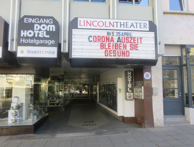 Außenansicht des Lincoln Theaters in Berlin, Deutschland, mit Glasfenstern und -türen sowie einer Tafel und einer belebten Stadtlandschaft im Inneren.