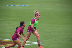 Zwei Frauen beim Fußballspielen auf einem Feld, eine in einem grünen T-Shirt und Shorts, die andere in einem pinken Kleid.