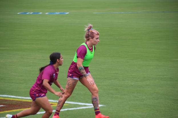 Zwei Frauen beim Fußballspielen auf einem Feld, eine in einem grünen T-Shirt und Shorts, die andere in einem pinken Kleid.