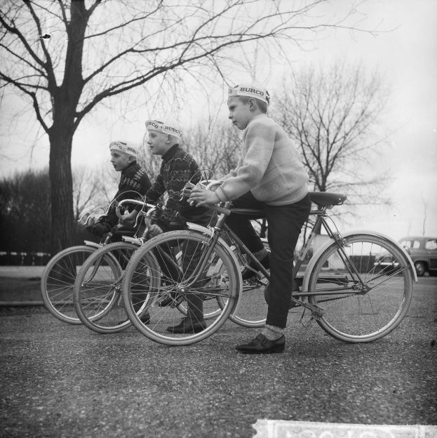 Drei Jungs auf Fahrrädern die Straße entlang mit einem Auto im Hintergrund, in Schwarz-Weiß.