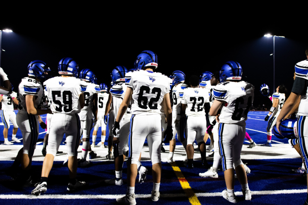 Eine Gruppe von Füßballspielern in Helmen und Stiefeln steht auf einem Feld, mit Flutlichtmästchen im Hintergrund.