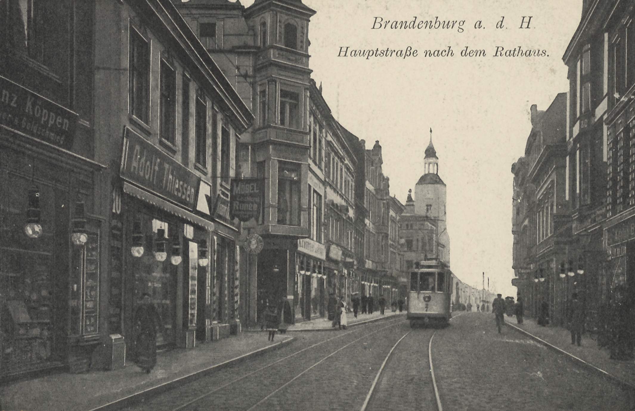 Schwarzes und weißes Foto einer Stadtstraße in Brandenburg, Deutschland mit einer Straßenbahn, Passanten, Gebäuden, Schildern, Straßenlaternen und einem bewölkten Himmel.