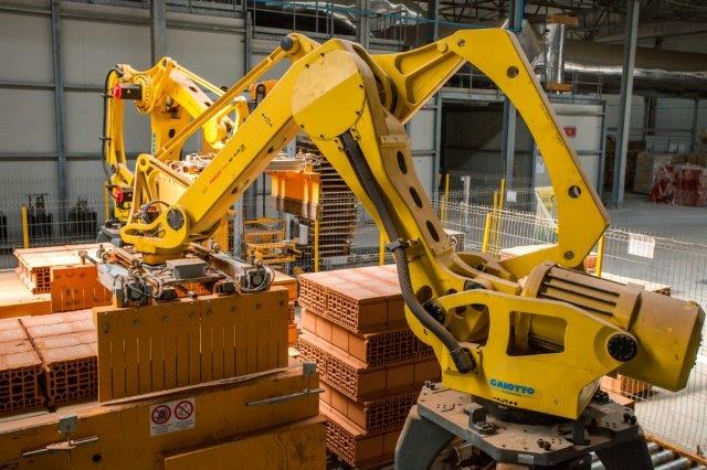 Großes Industrie-Lager mit gestapelten Kisten, Kranen, Zaun, Pfählen und einer fernen Wand in einer Fertigungsumgebung.