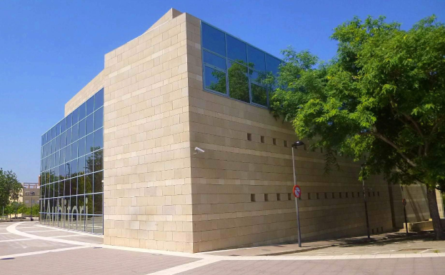 Großes Gebäude mit zahlreichen Fenstern, als NSA-Hauptquartier identifiziert, umgeben von Straßeninfrastruktur, Kraftfahrzeugen, Bäumen und einem bewölkten Himmel.